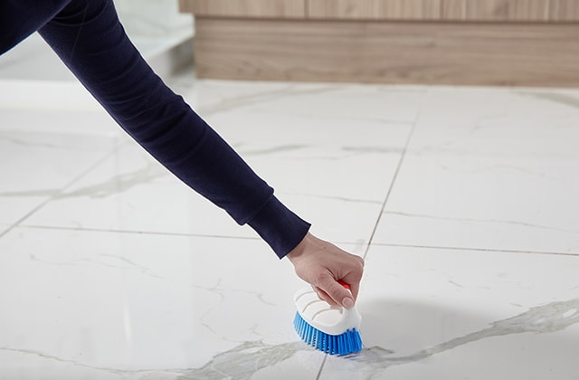Person cleaning a ceramic floor with a brush