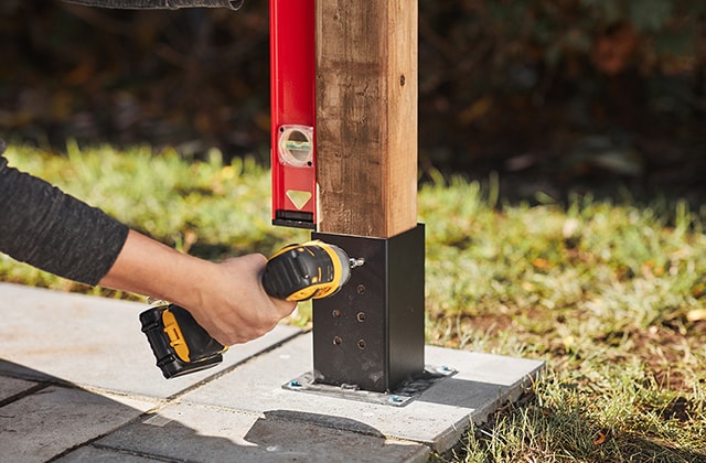 Person ensuring a wooden post is straight using a level