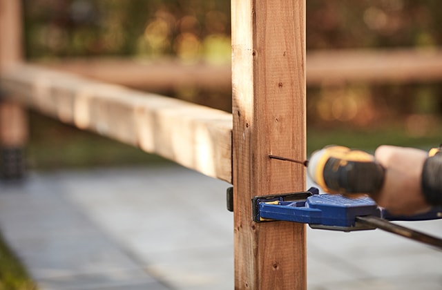 Person using a drill to secure the bottom crossbeam of a pergola