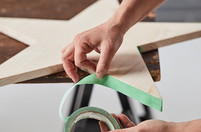 Person putting masking tape on a wooden star