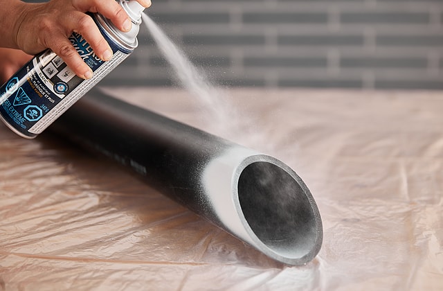 Person spraying white paint on a pipe
