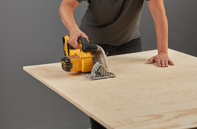 Person cutting a plywood sheet with a circular saw