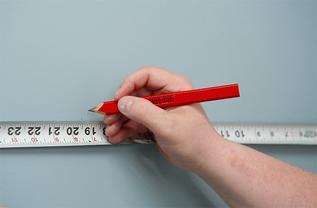 Person using a tape measure and a pencil on a wall