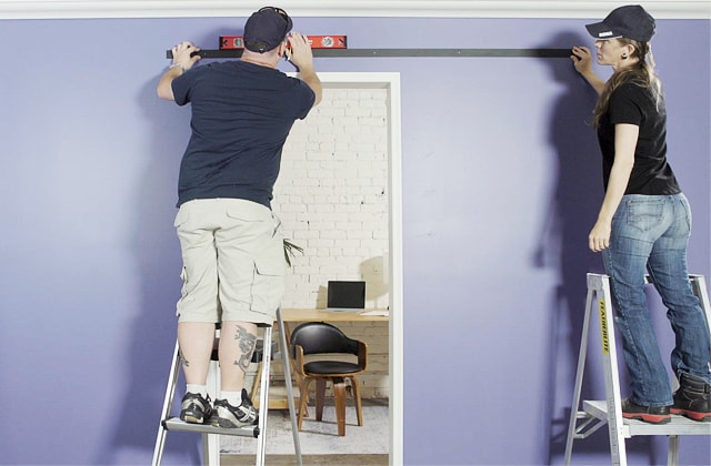 Two people installing  a barn door rail