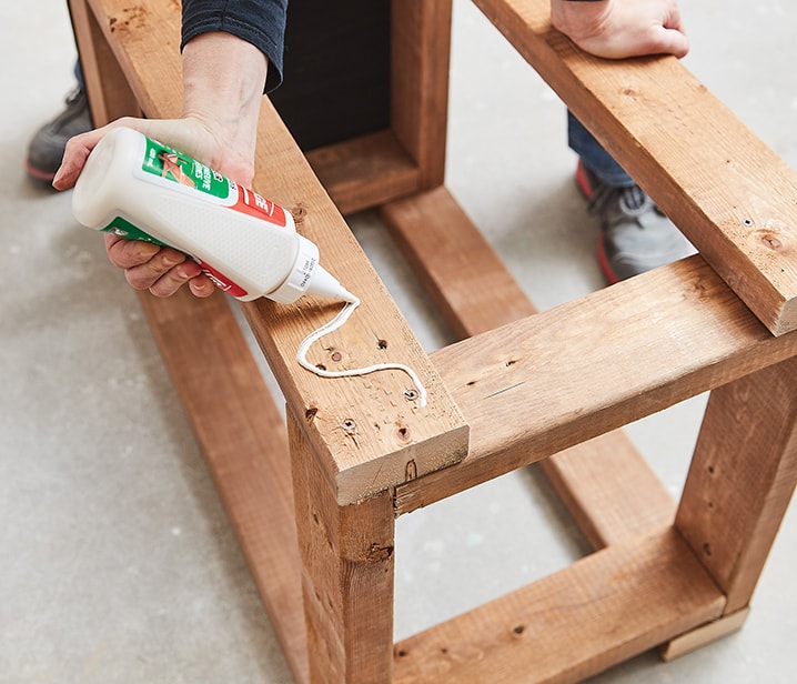 Woman applying wood glue to a wooden structure