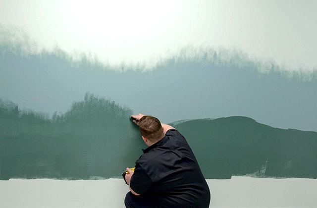 Person applying green paint on a wall