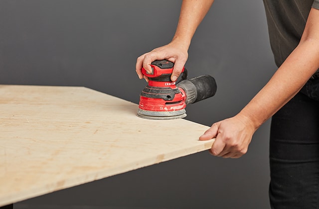 Person sanding a plywood sheet using a sander