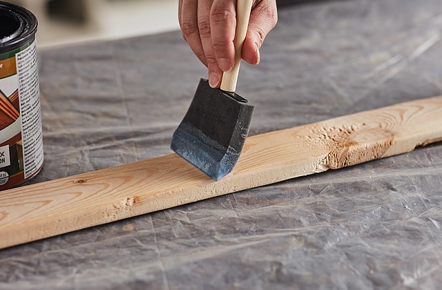 Person applying varnish to a piece of wood using a foam brush