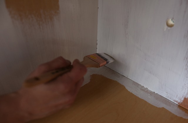 Person applying primer inside kitchen cabinets