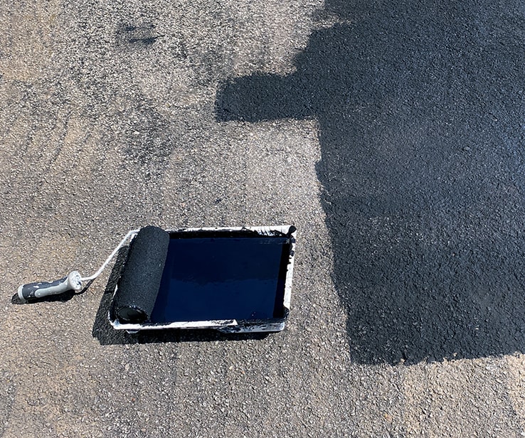 Rouleau à peinture et scellant sur une entrée d’asphalte Rouleau à peinture et scellant sur une entrée d’asphalte