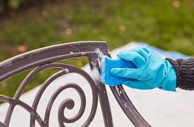 Person cleaning patio furniture with a sponge