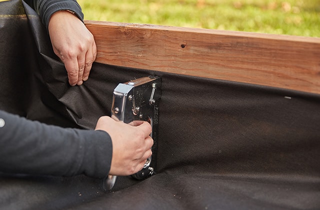 Person adding geotextile sheet to the bottom of a wooden sandbox