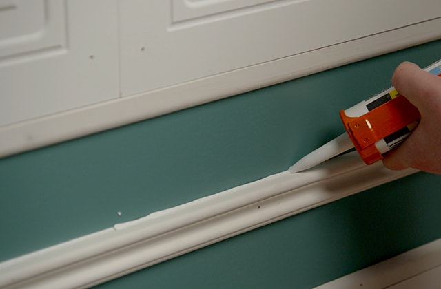 Person applying caulking along a baseboard