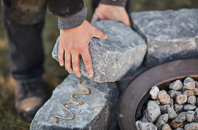 Person gluing the top row of a stone fire pit