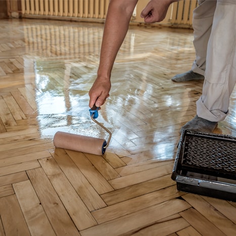 Person applying varnish on a wooden floor with a roller Person applying varnish on a wooden floor with a roller