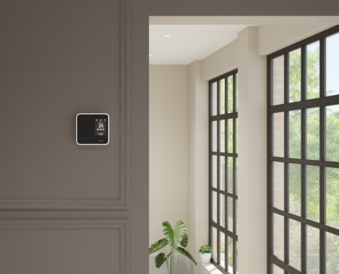 Black smart thermostat on a grey-brown wall