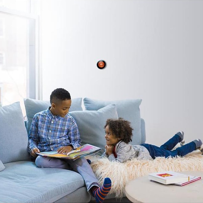 Kids playing on a couch with a thermostat on the wall