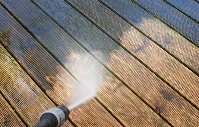 Person pressure washing a wooden deck
