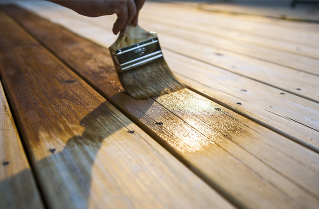 Personne appliquant de la teinture sur une terrasse en bois Personne appliquant de la teinture sur une terrasse en bois